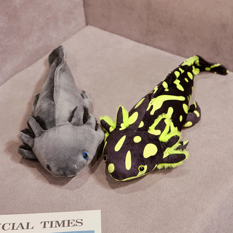 Cute Axolotl Plush Toy – Squishmallow Salamander Stuffed Animal Two plush axolotl toys on a beige fabric surface, one gray with blue eyes and the other black with bright neon yellow-green markings.