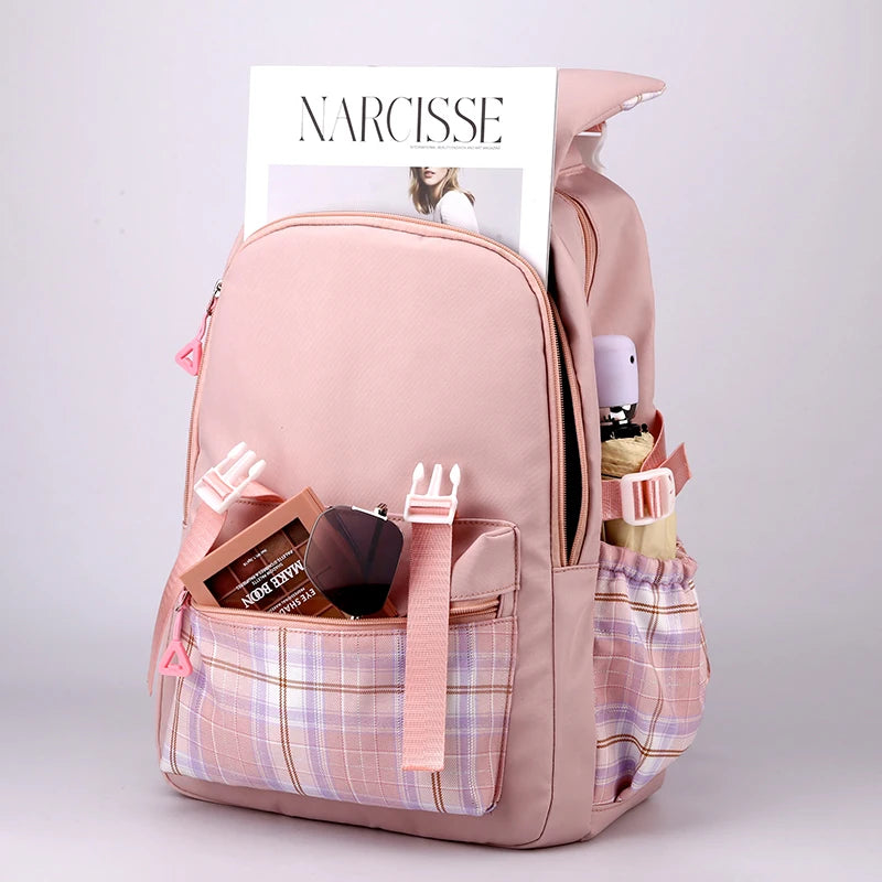 Capybara Bubble Tea Backpack – School Bag for Teens A light pink backpack with a plaid front pocket and side mesh pockets, shown on a light gray studio background with various items stuffed into it. A magazine titled NARCISSE is visible at the top.