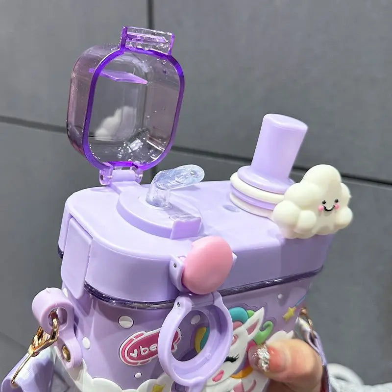 Capybara Kids Water Bottle – Cartoon Straw Cup A close-up of a pastel purple water bottle with a cute cloud charm, a small pink loop, and a clear lid, held by a hand against a gray tiled background.