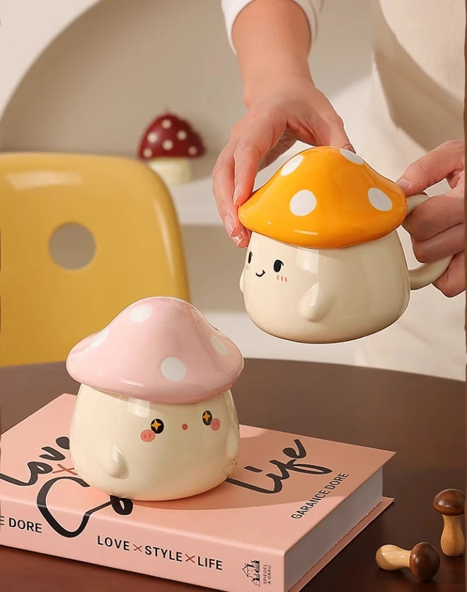 Cute Mushroom Coffee Mug with Lid – 400ML Ceramic Cup Two cute mushroom-shaped mugs on a book with a person holding one of them.