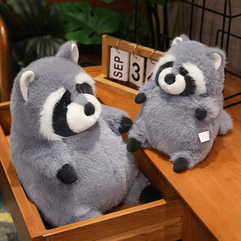 Squishmallow Grey Raccoon Plush Toy Stuffed Animal Two plush raccoons on a wooden surface with a calendar in the background