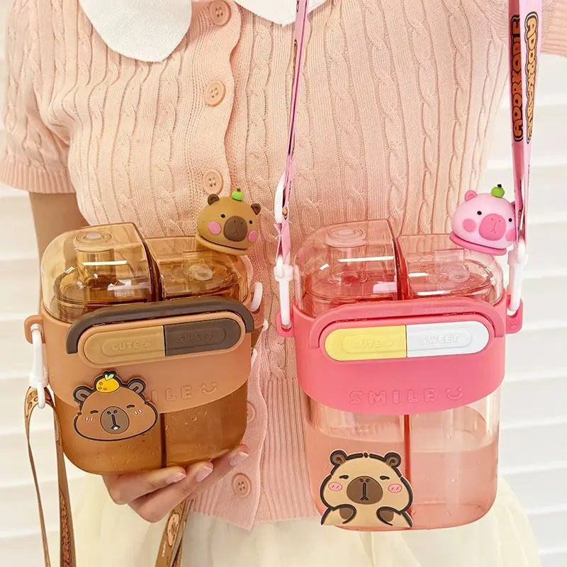 Cute Capybara Kids Water Bottle – Large Capacity Straw Cup Two cute water bottles with bear-themed covers, shown being held by a person wearing a pink cardigan. One bottle is brown with a brown bear cover, and the other is pink with a pink bear cover.