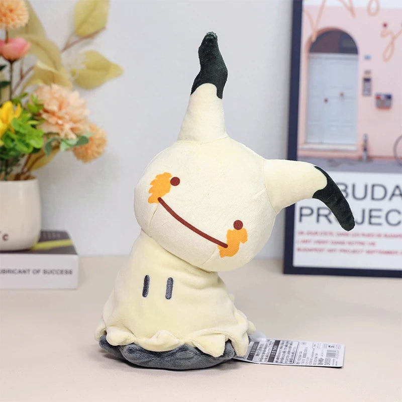 Pokemon Mimikyu Plush – Shiny Stuffed Toy Plush toy resembling a cartoon character on a table with flowers and a picture frame in the background.