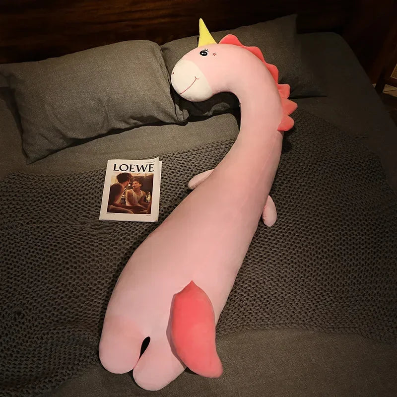 Squishmallow Fluffy Animal Body Pillow Pink dragon plush toy on a dark surface with a Loewe magazine in the background
