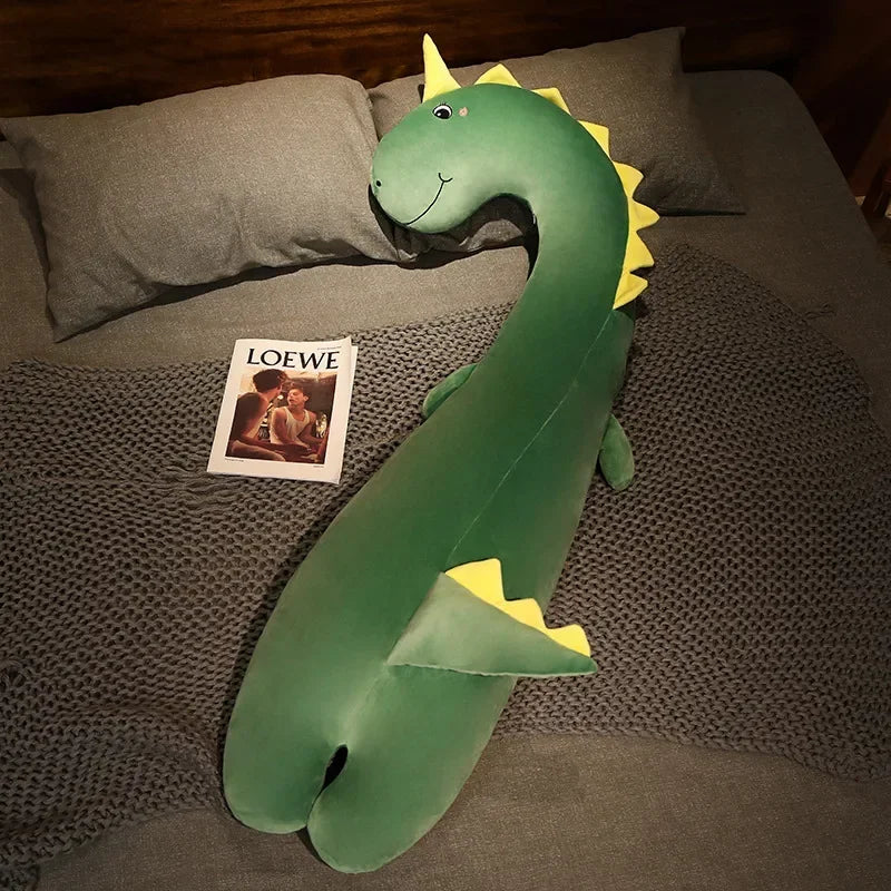 Squishmallow Fluffy Animal Body Pillow Green dinosaur plush toy on a bed with a LOEWE magazine