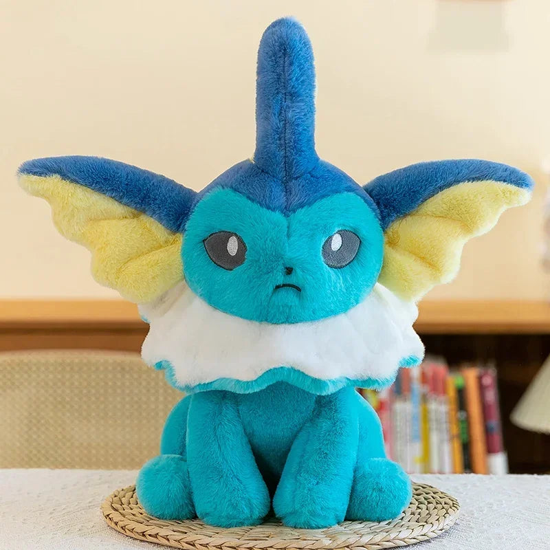 Pokemon Eevee Plush Toy – Vaporeon, Flareon & Jolteon Soft Stuffed Animal A blue and yellow plush toy with a white ruffled collar, sitting on a woven mat on a white table with a blurred indoor background.