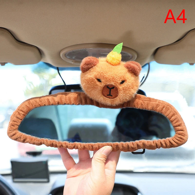 Capybara Car Headrest Neck Pillow & Tissue Holder – Plush Car Decor Car mirror cover with bear design held by a hand inside a vehicle.