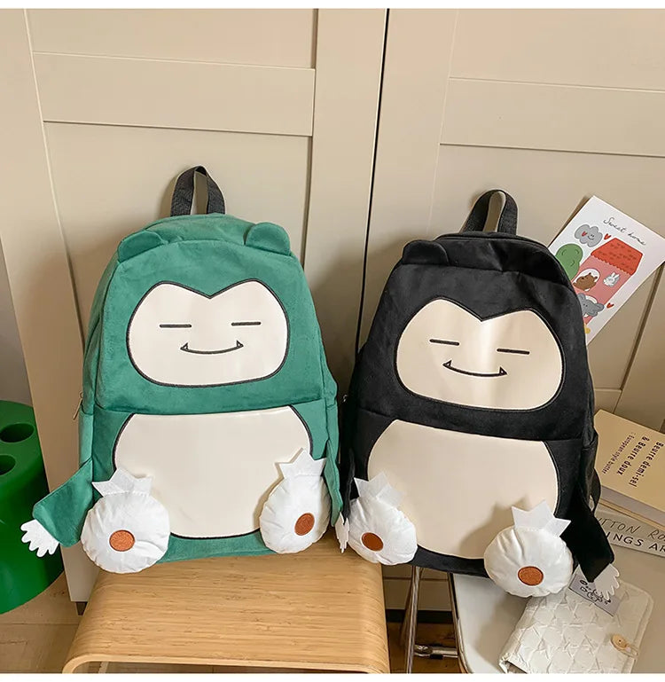 Snorlax Pokemon Backpack Large Capacity Casual Bag Two plush character backpacks styled like penguins, one in mint green and one in black, displayed on a wooden stool in front of beige cabinets.