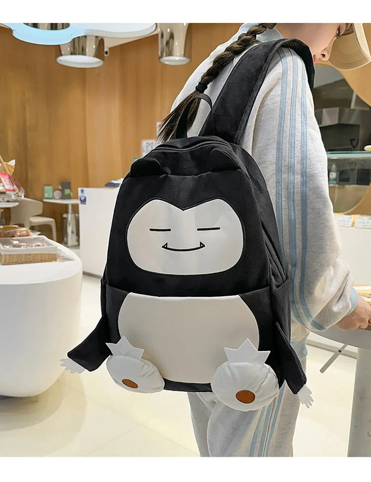 Snorlax Pokemon Backpack Large Capacity Casual Bag A person wearing a black and white penguin backpack in a modern indoor retail environment. The backpack features a cute cartoon penguin face and penguin feet details.