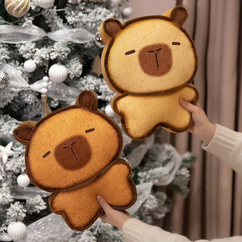 Capybara Bread Pillow – Cute Toast Plush Cushion Two bear-shaped bread toys held by hands in front of a decorated Christmas tree.