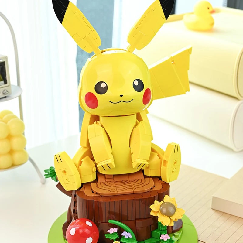 Pokemon Pikachu Building Blocks – DIY Model Brick Toy A yellow Pikachu-themed toy or model figure with large black-tipped ears, red cheek circles, and a smiling face, posed on a brown log base with small green, red, yellow, and pink decorative details in a bright indoor setting.