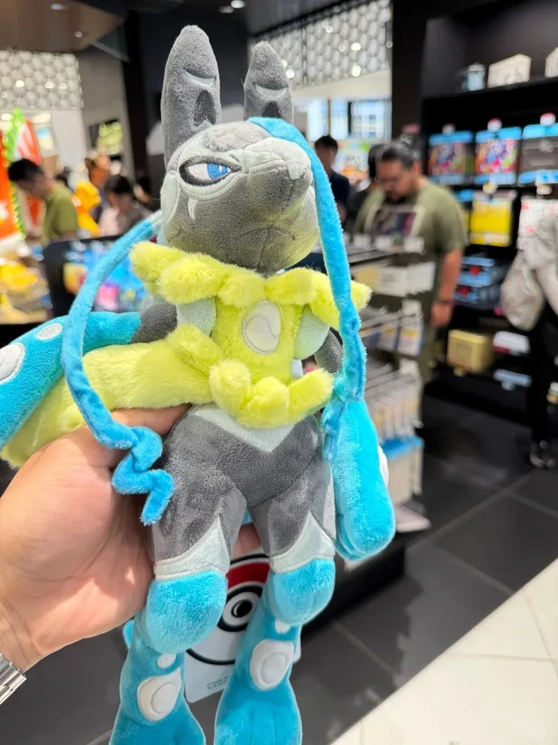 Pokemon Mega Plush Toy – Mega Lucario, Mega Greninja & Mega Starmie A plush toy of a gray and blue creature with yellow accents, held up by a hand in a retail store setting.