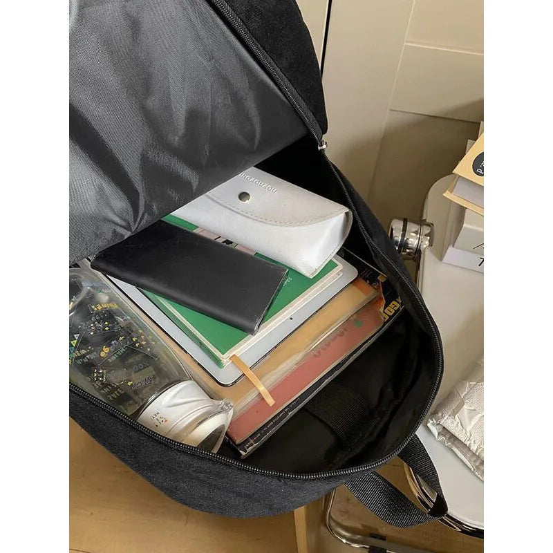 Snorlax Pokemon Backpack Large Capacity Casual Bag An open black backpack shown from above, filled with a white pouch, black wallet, notebooks, and other small accessories, photographed indoors near a desk or shelf.