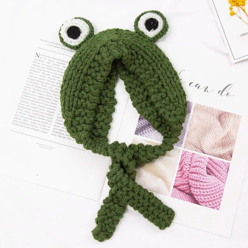 Cute Green Frog Crochet Beanie Hat – Knitted Winter Costume Cap Green knitted frog scarf on a white surface with a magazine in the background