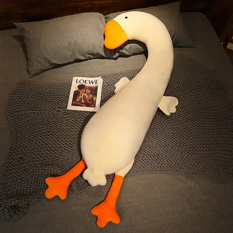 Squishmallow Fluffy Animal Body Pillow Plush goose toy on a bed with a magazine underneath