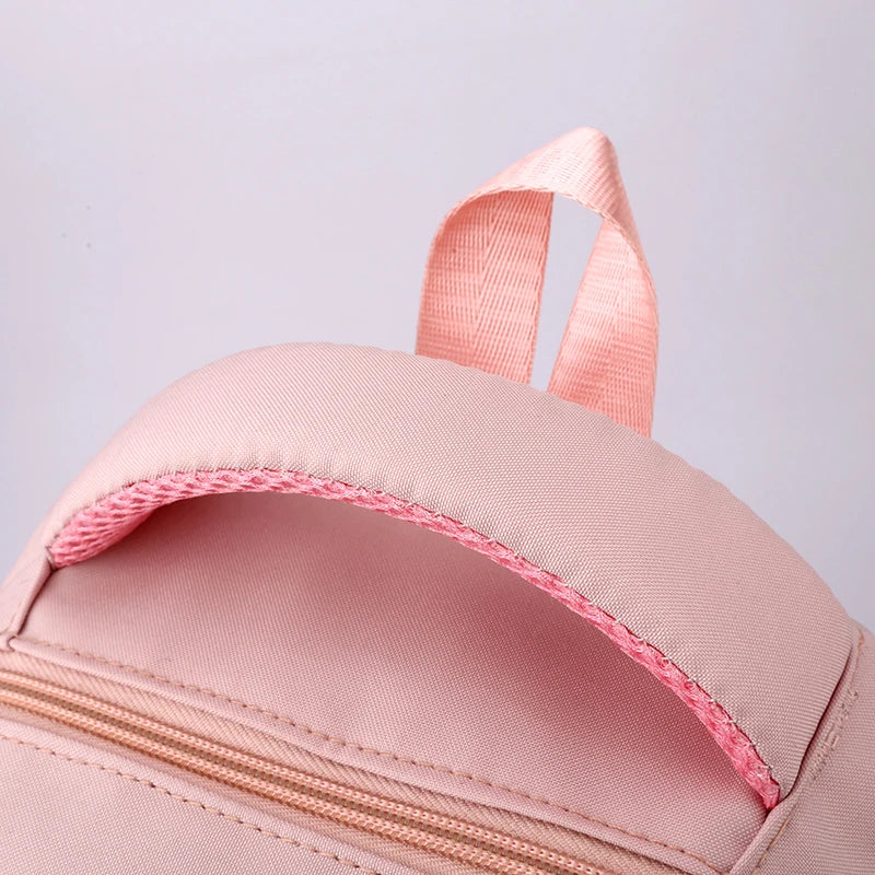 Capybara Bubble Tea Backpack – School Bag for Teens Close-up of a light pink fabric backpack showing the top handle, zipper, and stitched edge against a pale background.