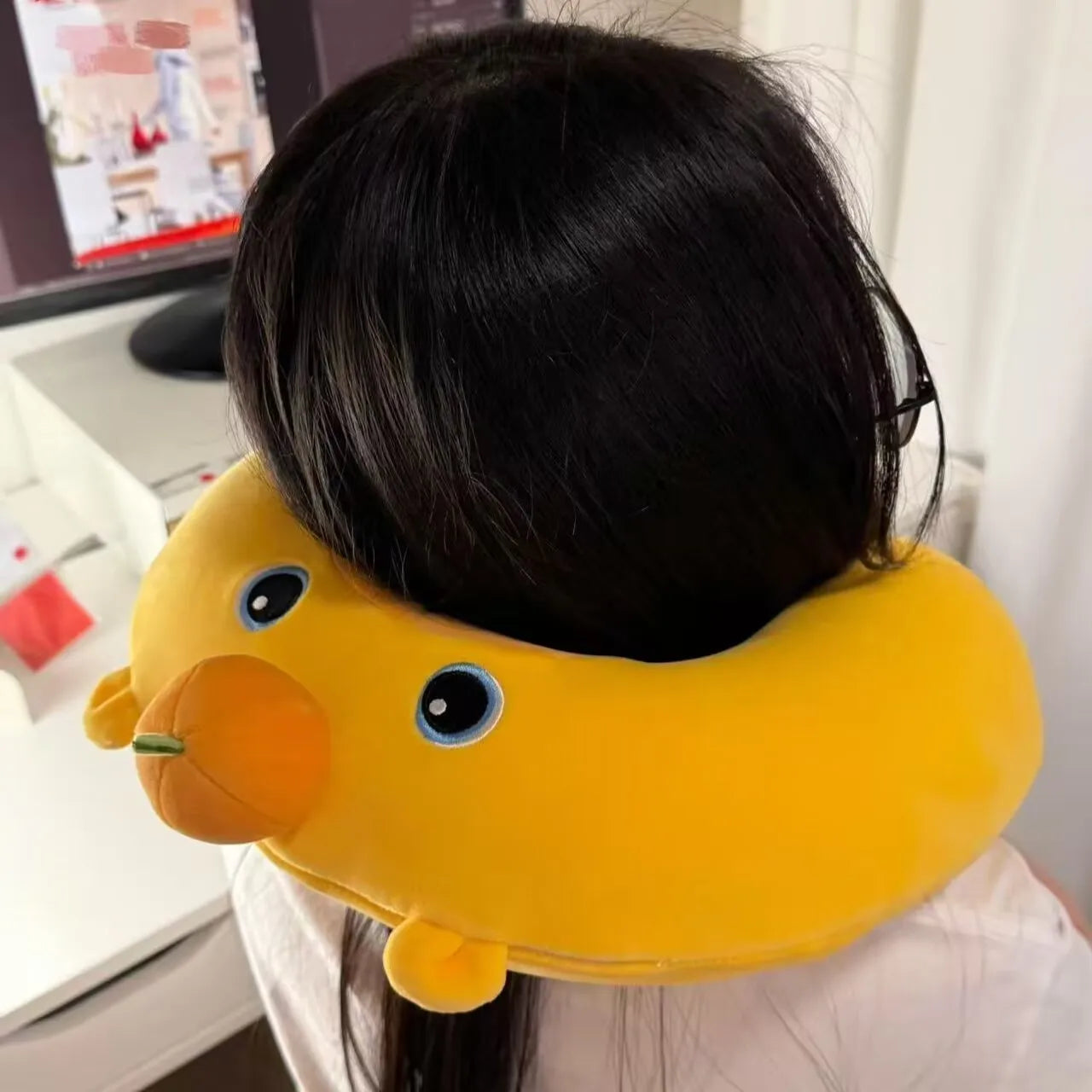 Cute Capybara U-Shaped Neck Pillow – Plush Travel Pillow A person viewed from behind wearing a yellow duck-shaped neck pillow with embroidered eyes and a small orange beak detail, in an indoor room setting.