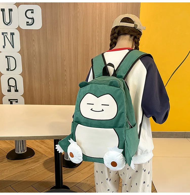 Snorlax Pokemon Backpack Large Capacity Casual Bag A person wearing a white and navy sweatshirt, patterned pajama pants, and a beige cap, viewed from behind while wearing a green and white cartoon character backpack with plush feet.