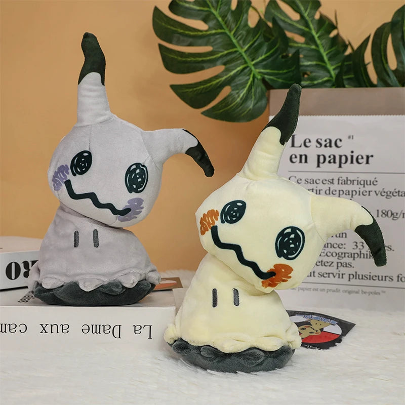 Pokemon Mimikyu Plush – Shiny Stuffed Toy Two plush Mimikyu character toys displayed on a tabletop with decorative books and a green plant leaf in the background.