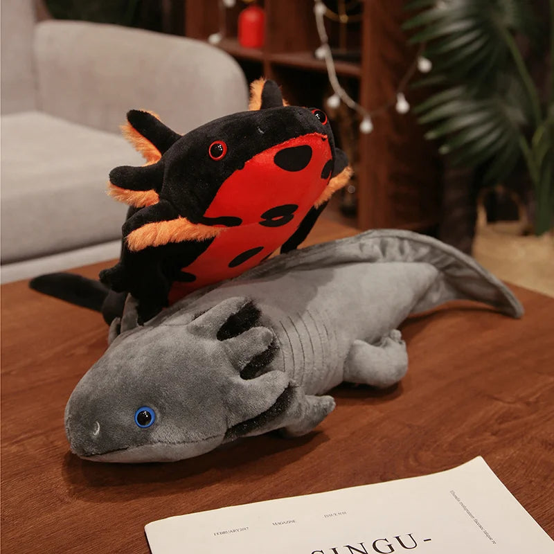 Cute Axolotl Plush Toy – Squishmallow Salamander Stuffed Animal Two plush toy axolotl fish arranged on a wooden table in a living room setting, with one black and red plush on top of a larger gray plush.
