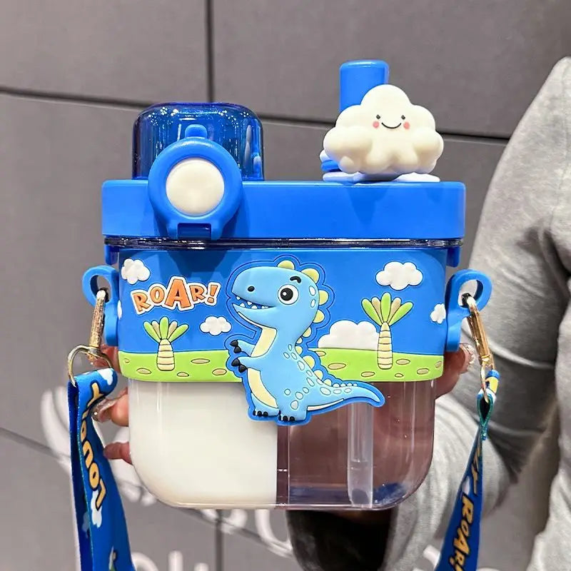 Capybara Kids Water Bottle – Cartoon Straw Cup A blue and clear plastic water bottle with a cartoon dinosaur design, held by a person. The bottle features a blue lid with a white cloud-shaped spout, a blue carrying strap, and a clear lower section containing a white liquid.