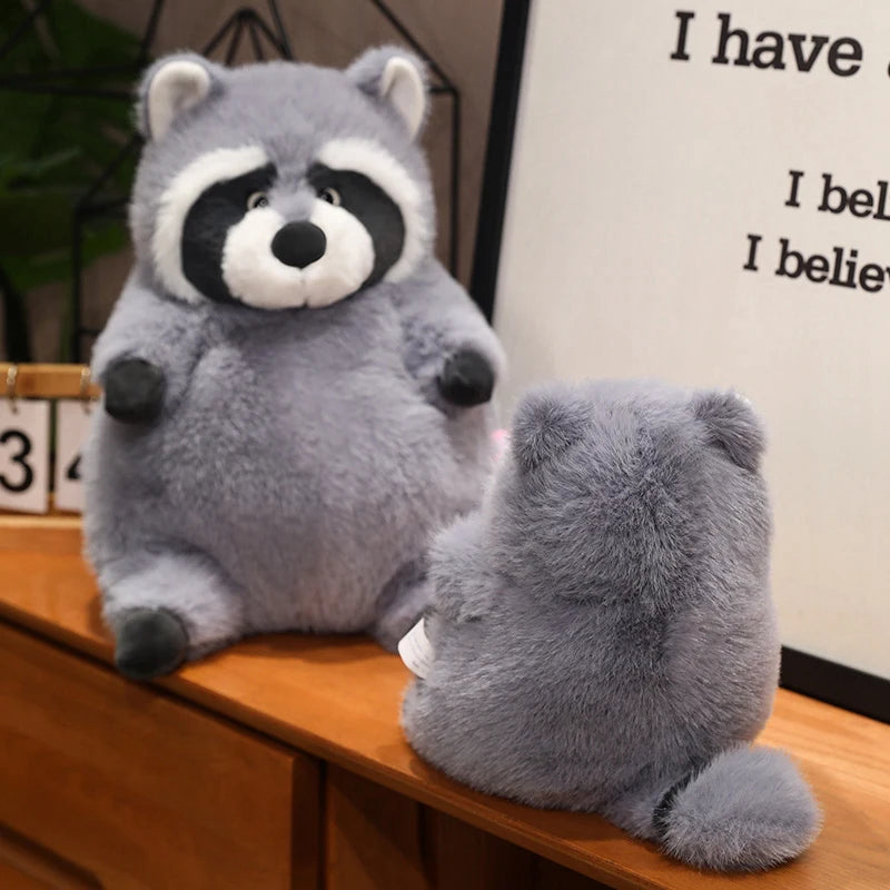 Squishmallow Grey Raccoon Plush Toy Stuffed Animal Plush raccoon toy sitting on a wooden surface with a motivational poster in the background.