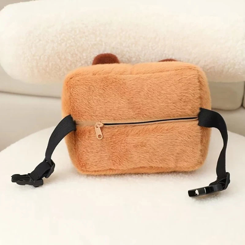 Capybara Car Headrest Neck Pillow & Tissue Holder – Plush Car Decor A plush rectangular pouch in a warm peachy-brown faux fur material, featuring a horizontal zipper with a small gold pull and black adjustable straps on both sides, photographed on a soft white surface.