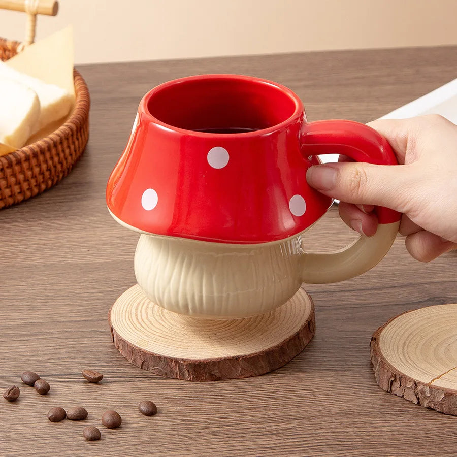 Premium Mushroom Coffee Cup – Large Ceramic Mug Red mushroom-shaped mug with white polka dots held by a hand on a wooden surface.