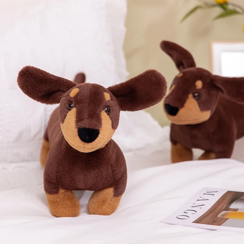 Realistic Dachshund Plush Dog Stuffed Animal Two plush dachshund toys on a white surface with a magazine underneath.
