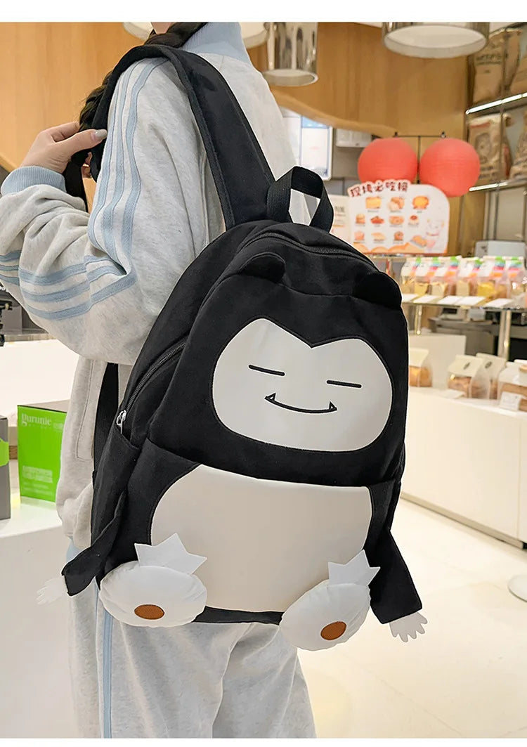 Snorlax Pokemon Backpack Large Capacity Casual Bag A person wearing a light gray tracksuit carries a black backpack shaped like the Pokémon character Cinnamoroll in a retail store setting.