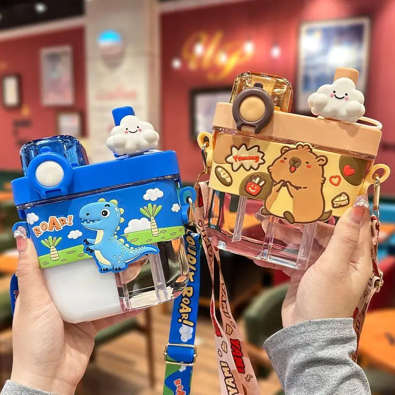 Capybara Kids Water Bottle – Cartoon Straw Cup Two cartoon water bottles held in hands, one blue with a dinosaur and the other beige with a bear, both with cloud charms and wrist straps in a cafe setting.