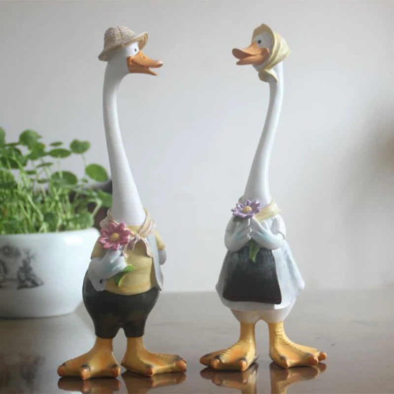 Resin Duck Family Garden Statue – Animal Outdoor Decor Sculpture Two decorative goose figurines with accessories on a reflective surface.