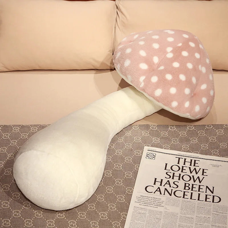 Large Mushroom Plush Pillow – Soft Huggable Stuffed Plant Cushion U-shaped body pillow with polka dot top on a couch next to a newspaper.