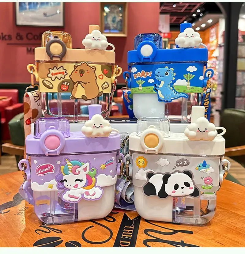 Capybara Kids Water Bottle – Cartoon Straw Cup Four children's water bottles with colorful cartoon designs, including a bear, dinosaur, unicorn, and panda, displayed on a wooden table in a cafe setting.