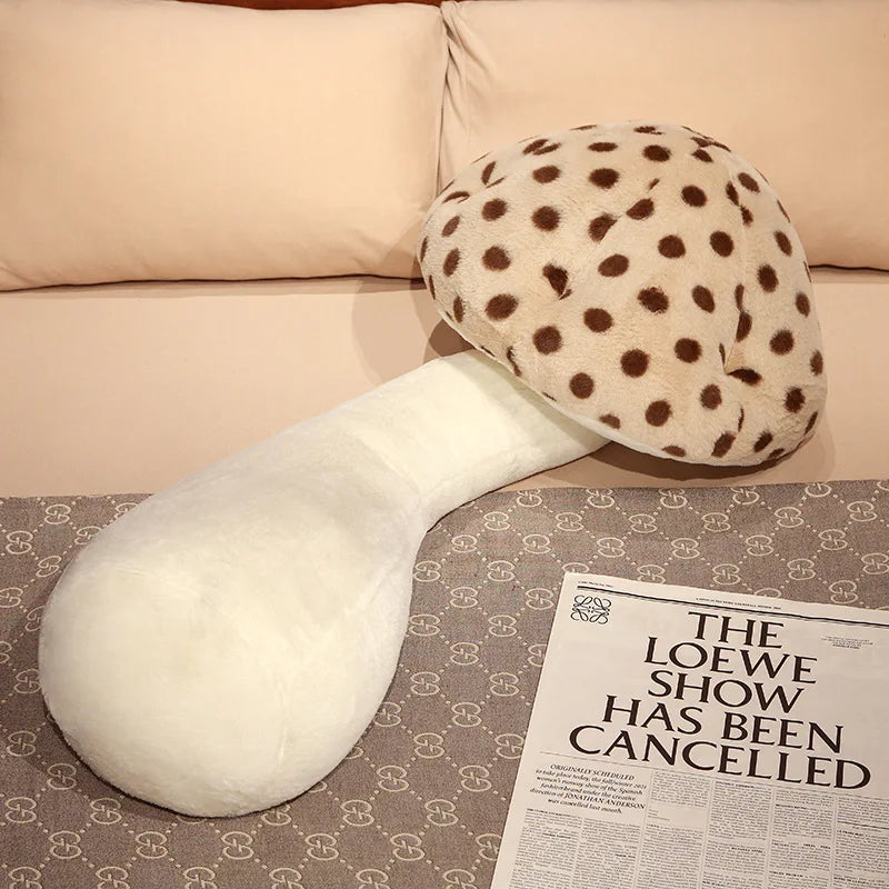 Large Mushroom Plush Pillow – Soft Huggable Stuffed Plant Cushion White and polka dot mushroom-shaped pillow on a patterned surface with a newspaper.