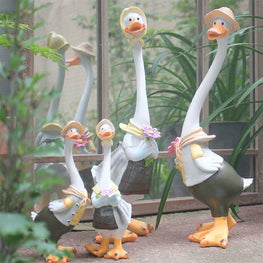Decorative goose figurines with hats and accessories in a garden setting