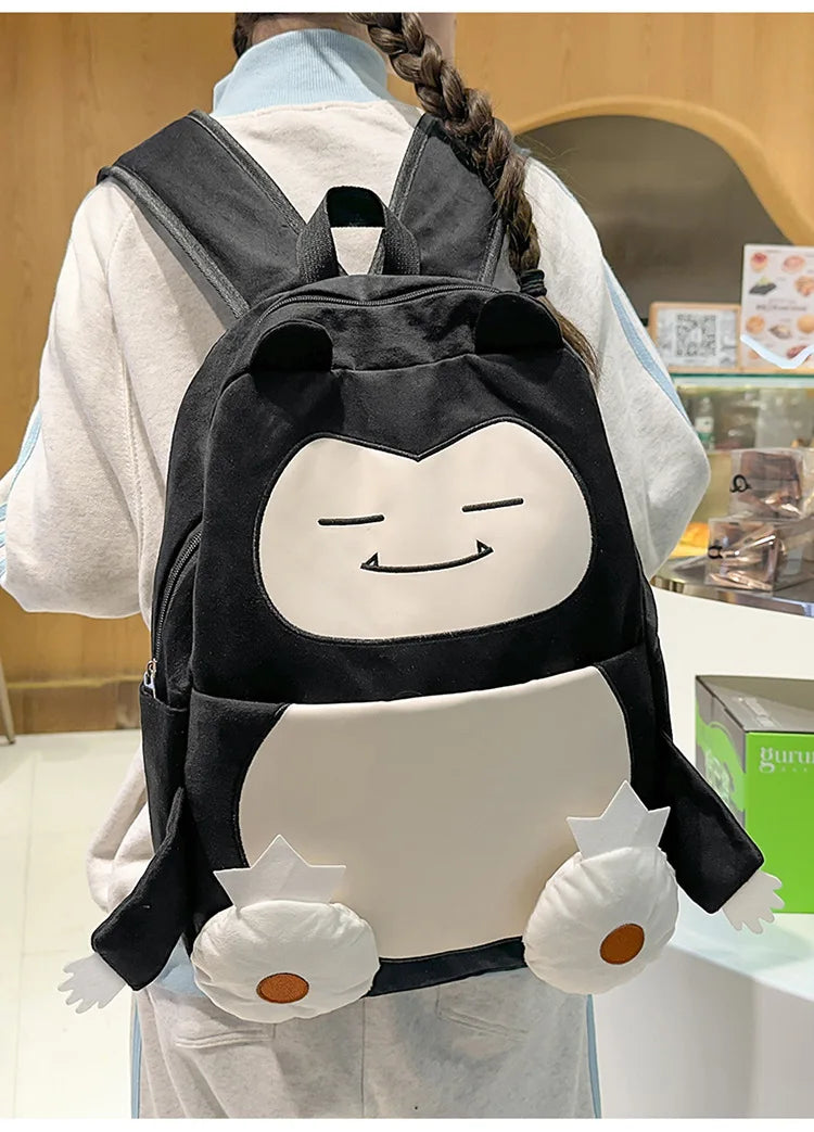 Snorlax Pokemon Backpack Large Capacity Casual Bag A person wearing a black and white penguin backpack with cute cartoon eyes and hands, photographed in a store setting.