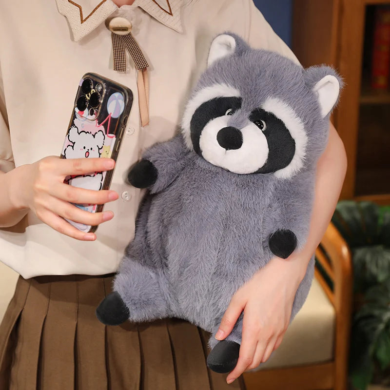 Squishmallow Grey Raccoon Plush Toy Stuffed Animal A gray plush raccoon toy being held by a person wearing a cream blouse and brown pleated skirt, while the person also holds a smartphone with a cartoon case.