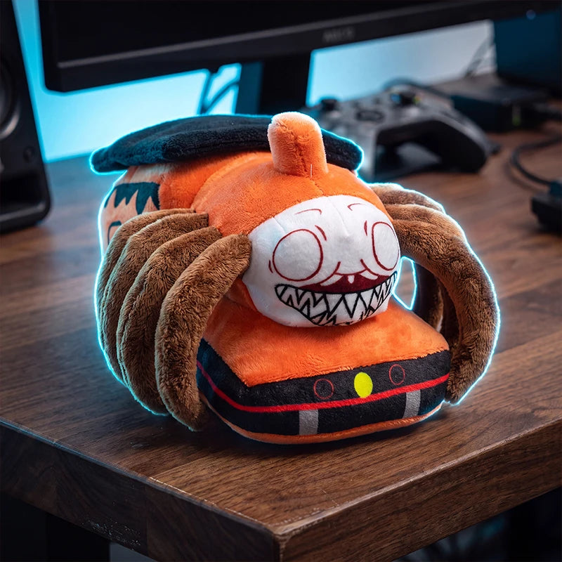 Horror Spider Plush Dolls – 2-Piece Creepy Halloween Set An orange plush toy shaped like a monster or creature with a white face, black details, and brown tentacle-like arms, resting on a wooden desk in front of a computer monitor and game controller.
