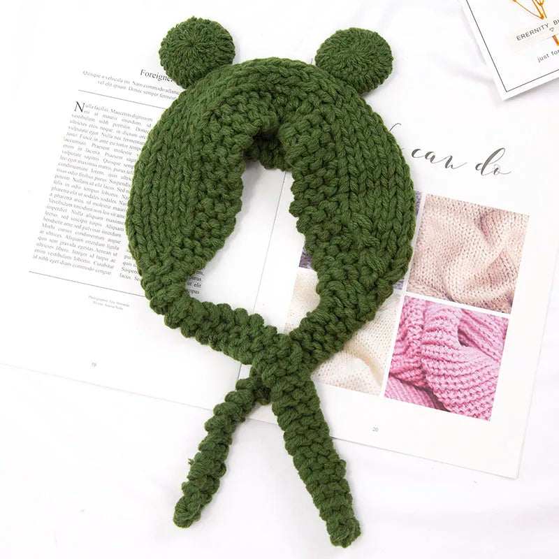 Cute Green Frog Crochet Beanie Hat – Knitted Winter Costume Cap Green knitted headband with pom-poms on a white surface with magazine pages.