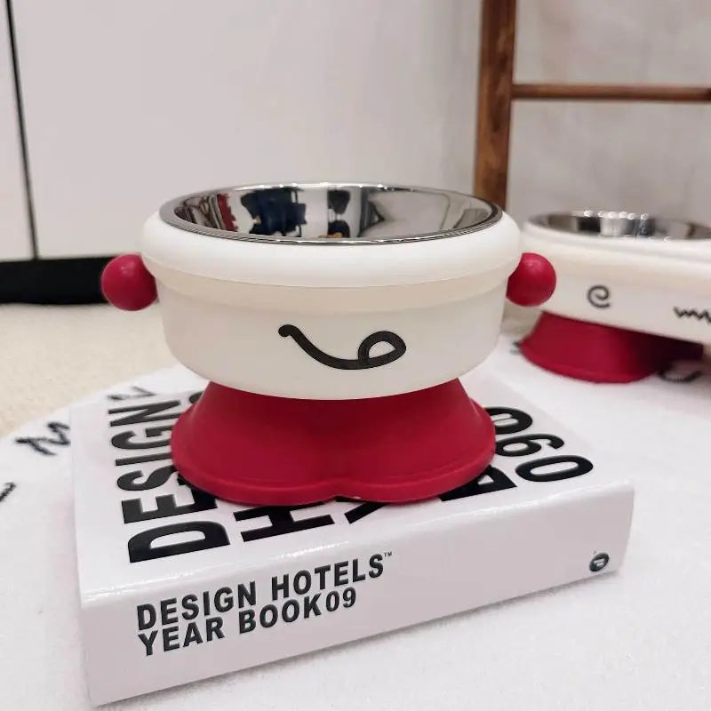 Elevated Pet Bowl Stainless Steel Anti-Slip Feeding Dish White and red pet bowl with a smiley face design on top of a book titled 'Design Hotels Year Book 09'.