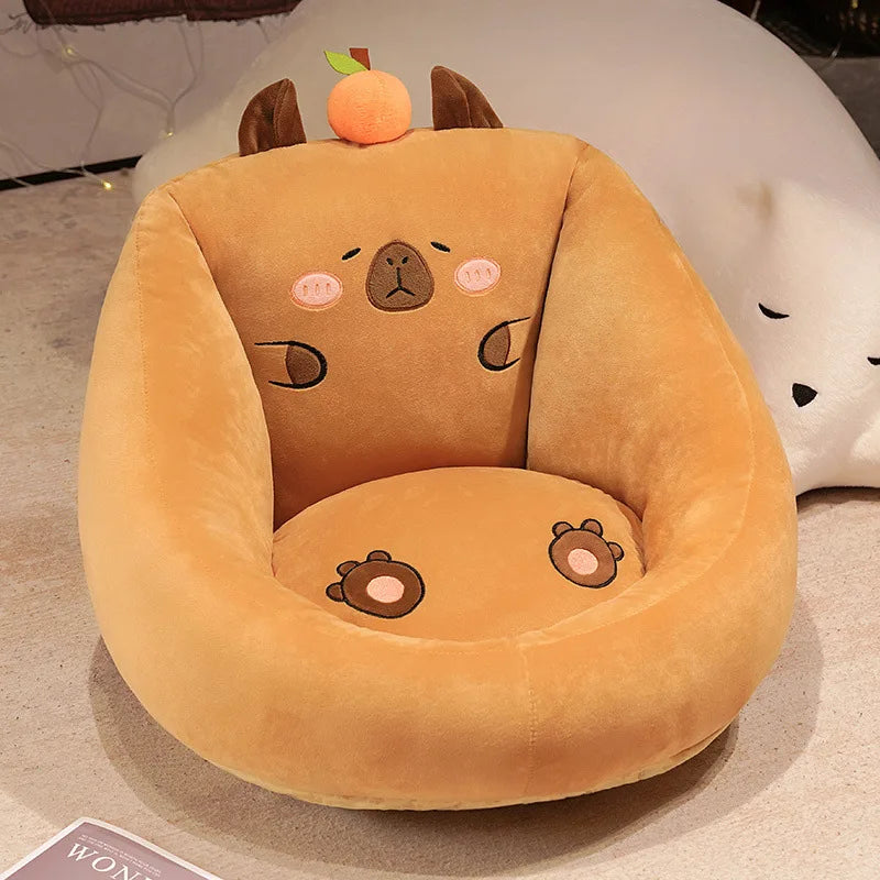 Capybara Floor Cushion – Futon Seat for Living Room & Bedroom A plush capybara-shaped armchair in warm camel brown, featuring embroidered facial details, small brown ears, a peach ornament on top, and matching cushioned seat and backrest.