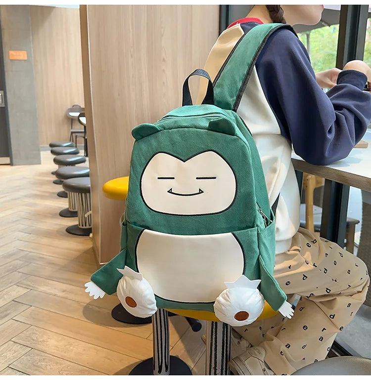 Snorlax Pokemon Backpack Large Capacity Casual Bag A green and white character backpack with a smiling face and small paw details, worn by a person sitting at a cafe table.