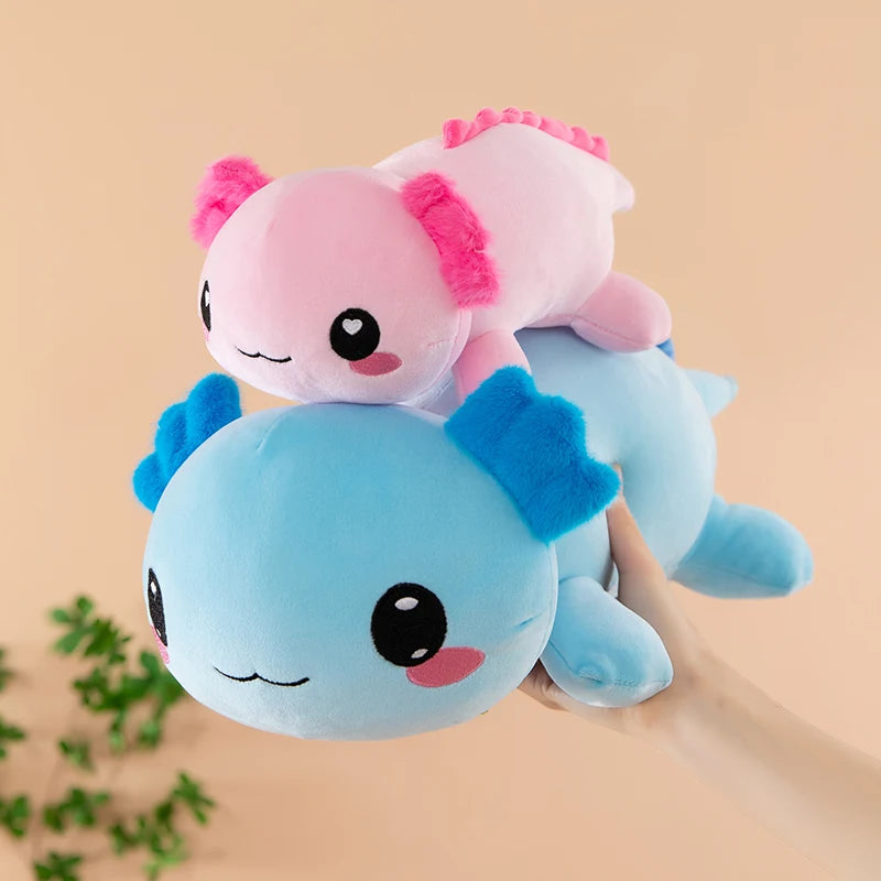 Axolotl Squishmallow Plush – Stuffed Animal Toy Two axolotl plush toys, one pink and one blue, on a beige background with green leaves.