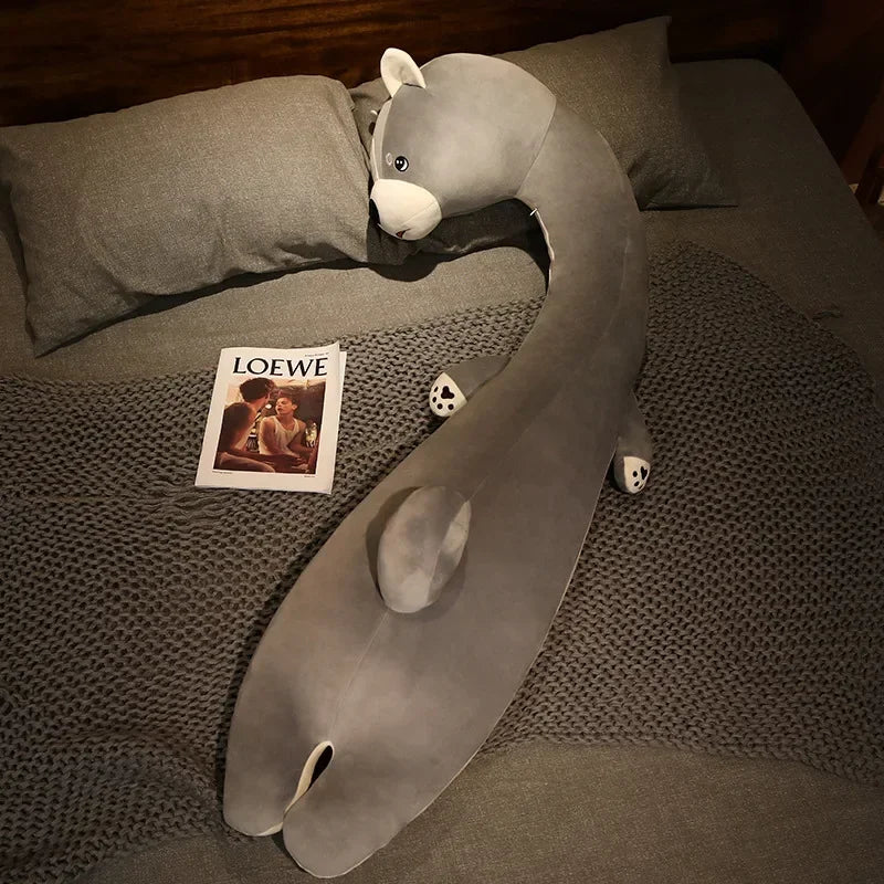 Squishmallow Fluffy Animal Body Pillow Gray plush toy resembling a snake on a bed with a Loewe magazine.