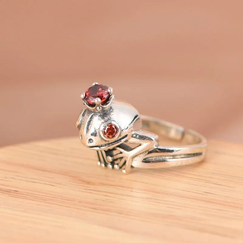925 Silver Frog Crown Ring – Retro Adjustable Statement Jewelry Silver frog-shaped ring with red gemstones on a wooden surface