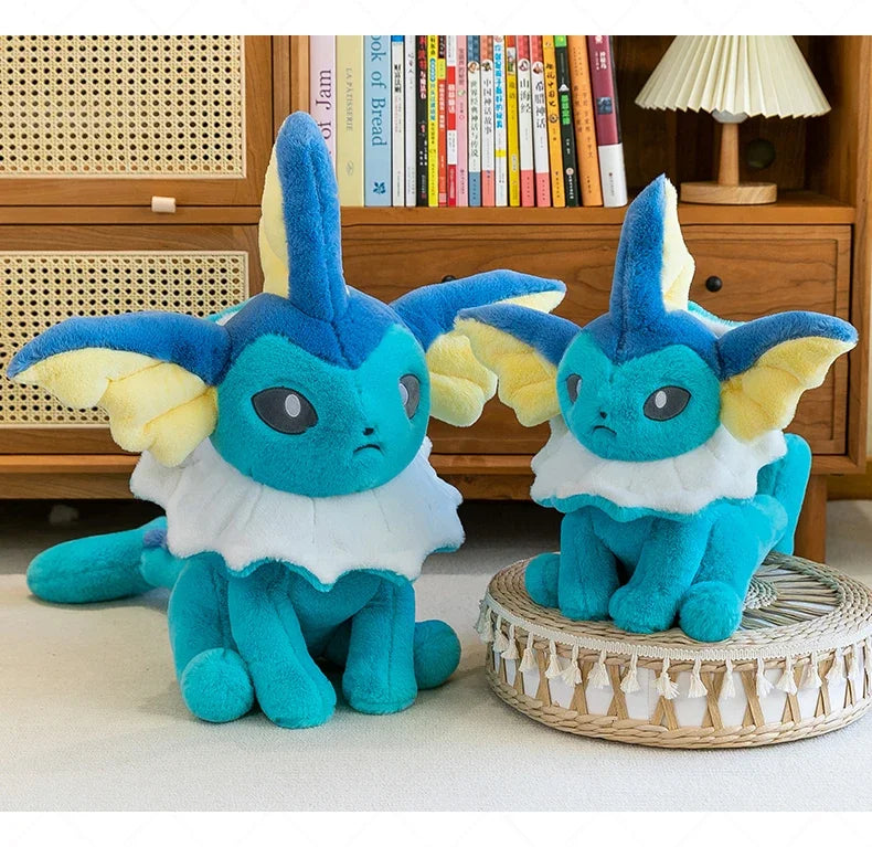 Pokemon Eevee Plush Toy – Vaporeon, Flareon & Jolteon Soft Stuffed Animal Two blue and yellow plush toy characters with white ruffled collars are posed indoors in front of a wooden bookshelf. One plush sits on the floor, and the other sits on a round woven cushion.