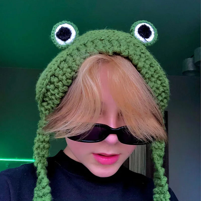 Cute Green Frog Crochet Beanie Hat – Knitted Winter Costume Cap Person wearing a green frog-themed knitted hat with large eyes and black pupils.