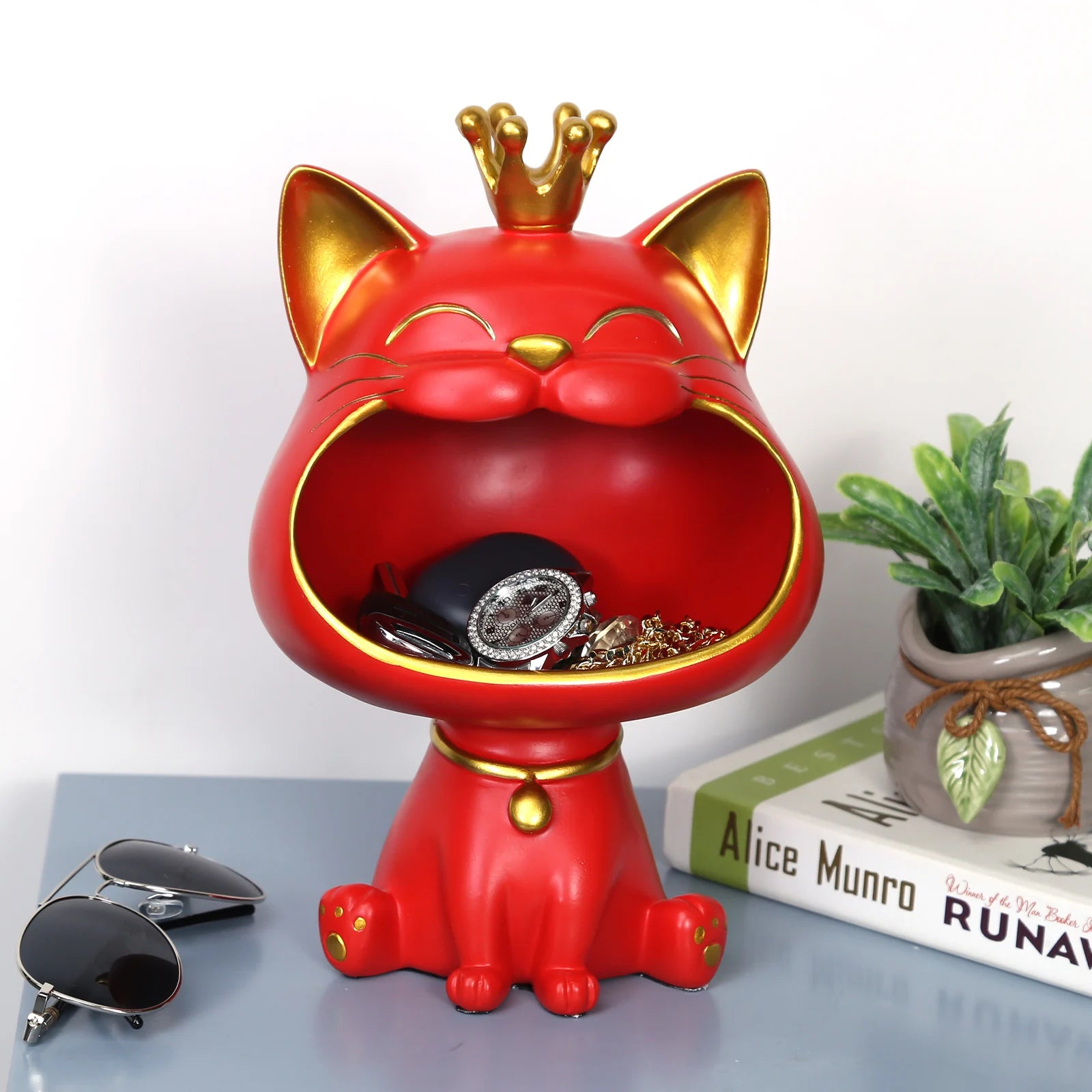Lucky Cat Figurine with Storage Box – Resin Laughing Cat Home Decor Red cat-shaped jewelry organizer with a gold crown on a surface with books and sunglasses.