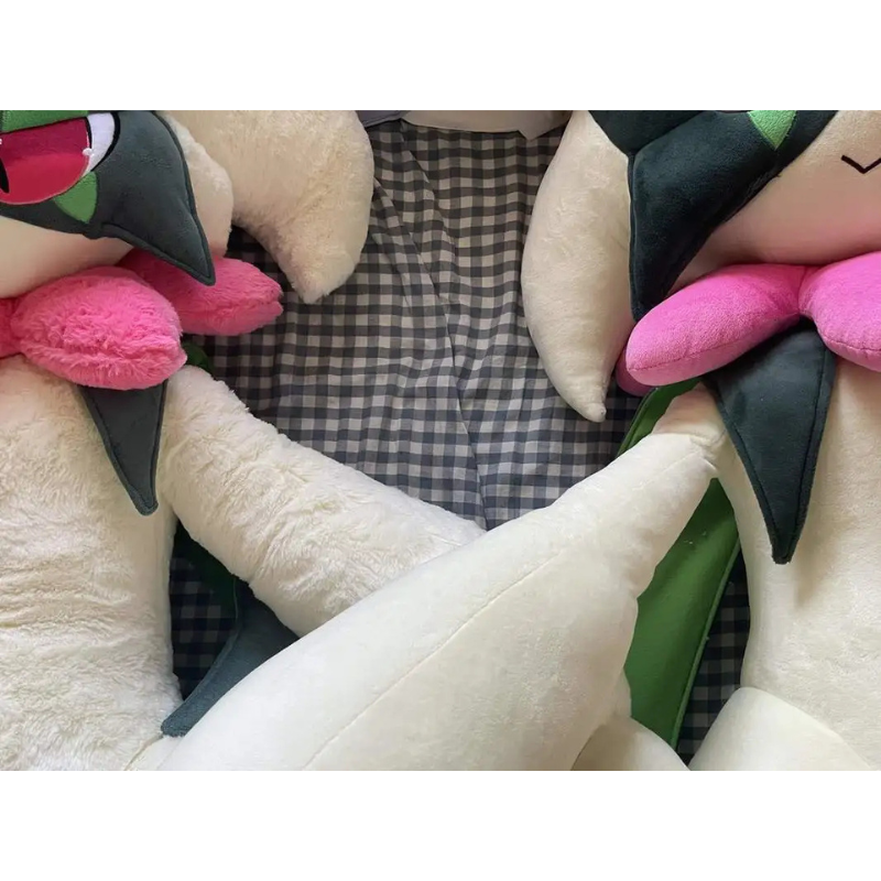 Pokemon Meowscarada Plush Pillow Stuffed Toy A close-up of a plush toy with cream-colored body, dark green leaf-like accents, and bright pink cheeks, arranged against a black-and-white checkered fabric background.